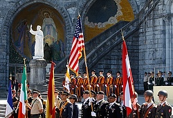 Military members stand near national flags during pilgrimage to Shrine of Our Lady of Lourdes in France