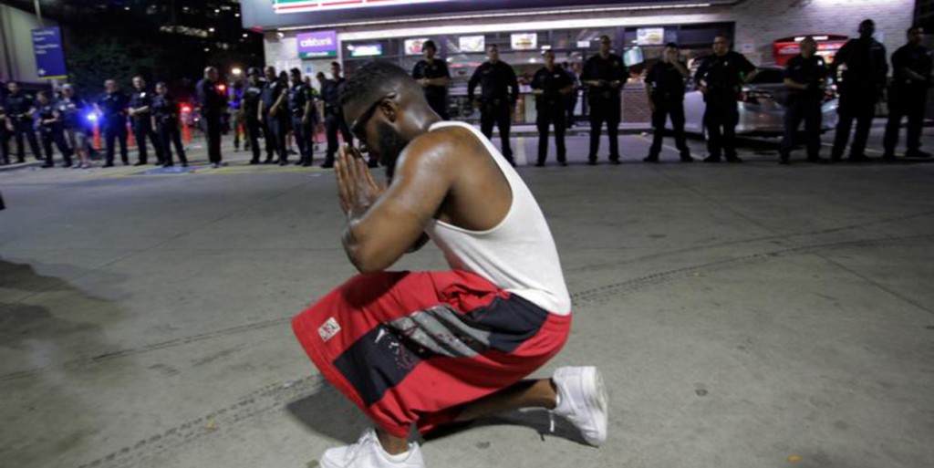 A protester prays near Dallas police officers July 7 after police officers were shot during a protest in Dallas. Snipers shot and killed five police officers and wounded seven more at the demonstration to protest the police killing of black men in Baton Rouge, La., and St. Paul, Minn. Two civilians also were injured in Dallas. (CNS photo/Ralph Lauer, EPA)