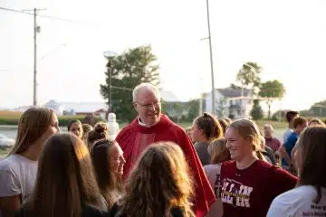 Priest wearing red stands among group of young women